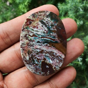 Puede incluir: Una gema ovalada con un patr&oacute;n de colores &uacute;nico. La piedra presenta una mezcla de tonos rojos, marrones, blancos y turquesas, creando un efecto veteado. La superficie pulida de la piedra refleja la luz, resaltando su belleza natural. Ideal para la creaci&oacute;n de joyas.