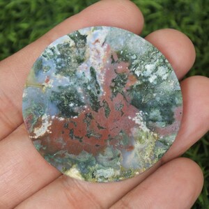 May include: A round, polished agate stone featuring a range of colours, including green, brown, white, and red. The stone has a distinctive, swirling pattern.