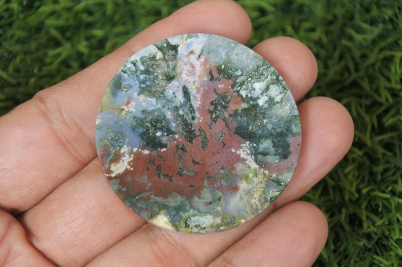 May include: A round, polished agate stone featuring a range of colours, including green, brown, white, and red. The stone has a distinctive, swirling pattern.