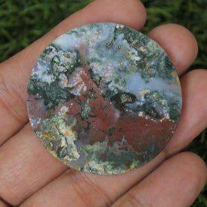 May include: A round, polished agate cabochon with a swirling pattern of green, brown, white, and grey. The stone has a natural, organic look.