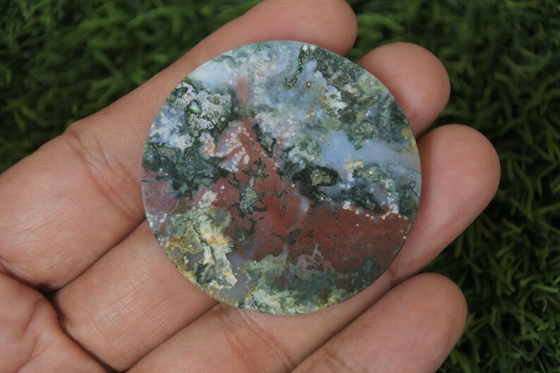 May include: A round, polished agate cabochon with a swirling pattern of green, brown, white, and grey. The stone has a natural, organic look.