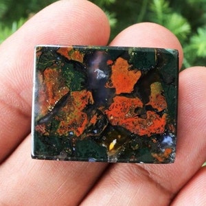 May include: A green, orange and brown agate cabochon with a polished, smooth surface. The stone has a unique, swirling pattern of colours.