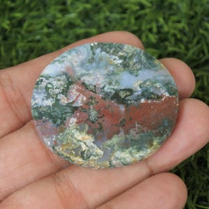 May include: A round, flat, green, red and white agate stone with a swirling pattern. The stone is approximately 5 cm in diameter.