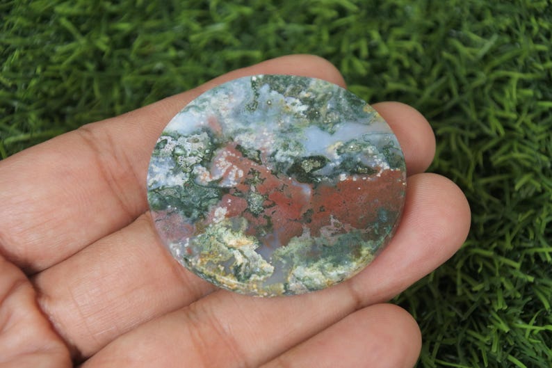 May include: A round, flat, green, red and white agate stone with a swirling pattern. The stone is approximately 5 cm in diameter.