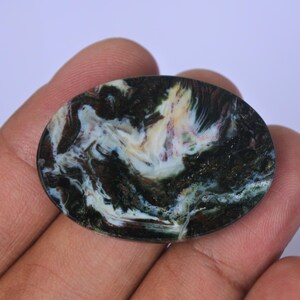 Pu&ograve; includere: Primo piano di una pietra di agata rotonda e lucidata con motivi a spirale di nero, bianco e verde.