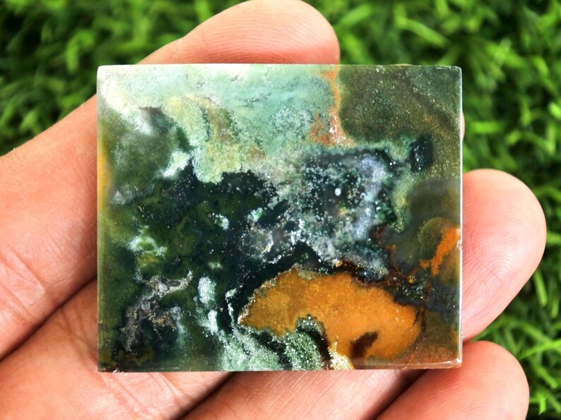 Peut inclure: Pierre pr&eacute;cieuse carr&eacute;e avec un motif unique de teintes vertes, brunes et orang&eacute;es. La pierre a une surface polie et un aspect naturel et terreux. Les couleurs se m&eacute;langent, cr&eacute;ant un design abstrait.