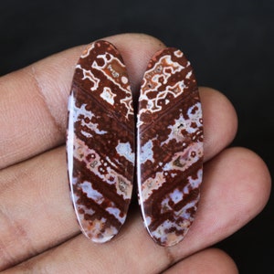 Może przedstawiać: Para owalnych kamieni szlachetnych w kształcie kaboszonu z brązowym, białym i czerwonym marmurowym wzorem.