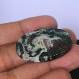 Pu&ograve; includere: Primo piano di una pietra di agata rotonda e ovale, lucidata, con un motivo a spirale di colori nero, bianco e marrone.