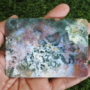May include: A rectangular slab of polished moss agate featuring a complex pattern of deep forest green, soft lavender, and earthy terracotta inclusions. The stone displays a smooth, flat surface with translucent areas and intricate mineral dendrites.