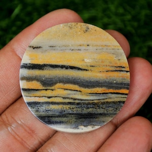 Pode incluir: Uma pedra redonda e polida com um padrão em camadas de preto, amarelo e branco. A pedra tem uma superfície lisa e polida.