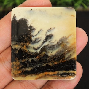 Peut inclure: Une pierre carrée et polie avec un motif unique. La pierre présente un mélange de couleurs, dont le noir, la crème et des nuances de brun et d'orange. Le motif évoque un paysage ou de l'art abstrait, avec des textures tourbillonnantes et superposées.