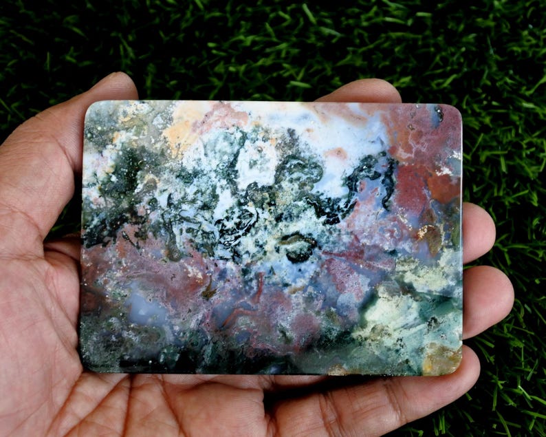 May include: A rectangular polished slab of moss agate featuring a complex pattern of deep forest green, earthy terracotta red, creamy white, and translucent grey inclusions. The stone has smooth, rounded corners and a flat, reflective surface.