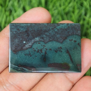 May include: A green and brown polished stone with a unique pattern. The stone is rectangular and has a smooth, glossy finish.