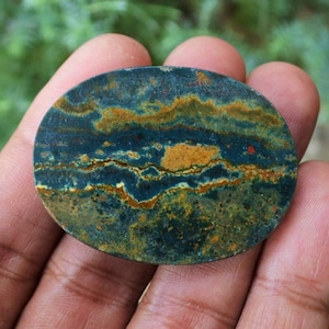 May include: Oval shaped green, blue, and gold jasper cabochon with a swirling pattern.
