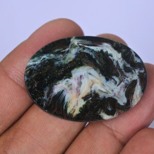 Pu&ograve; includere: Primo piano di un cabochon di agata nero, bianco e verde con motivi a spirale. Il cabochon &egrave; liscio e lucido, ed &egrave; tenuto in una mano.