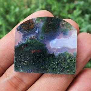 May include: A green, white, and brown moss agate cabochon with a polished, smooth surface. The stone has a unique, swirling pattern of colors and textures.