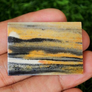 Puede incluir: Una losa rectangular de ágata bandeada con rayas negras, blancas y amarillas. La ágata tiene una superficie pulida y es adecuada para su uso en joyería o artesanía.
