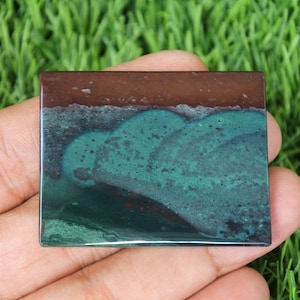 May include: A green and brown polished stone with a unique pattern. The stone is rectangular and has a smooth surface.
