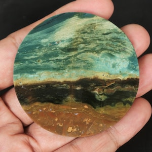 May include: A round, polished stone with a layered pattern of green, brown, and gold. The stone has a natural, organic look.