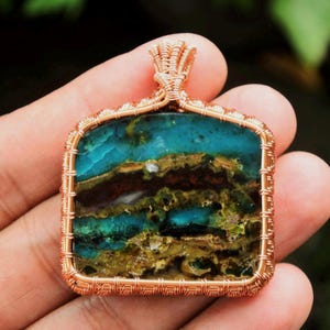 May include: A copper wire wrapped pendant featuring a square shaped, multi-colored stone with shades of blue, green, brown, and white.