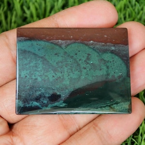 May include: A green and brown polished stone with a unique pattern. The stone is rectangular and has a smooth, glossy finish.