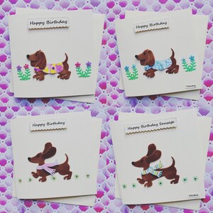 May include: Four handmade greeting cards featuring a brown dachshund dog with different coloured scarves and flowers. The cards say "Happy Birthday" and "Happy Birthday Sausage".