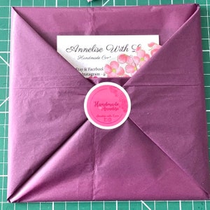 May include: A purple tissue paper envelope with a white sticker that says "Handmade Annelise" and "Annelise with Love EO". The envelope has a white card inside with the text "Annelise With Love Handmade Cor' Etsy & Facebook Instagram - @"