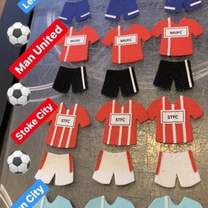 May include: A set of felt football jerseys and shorts in red, white, and black with team names "MUFC" and "STFC".