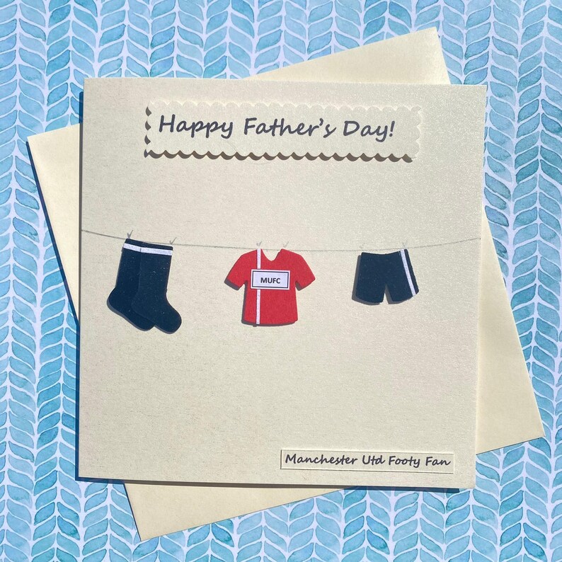 May include: A card with the text "Happy Father's Day!" and a drawing of a football jersey, shorts, and socks hanging on a clothesline. The text "Manchester Utd Footy Fan" is at the bottom of the card.
