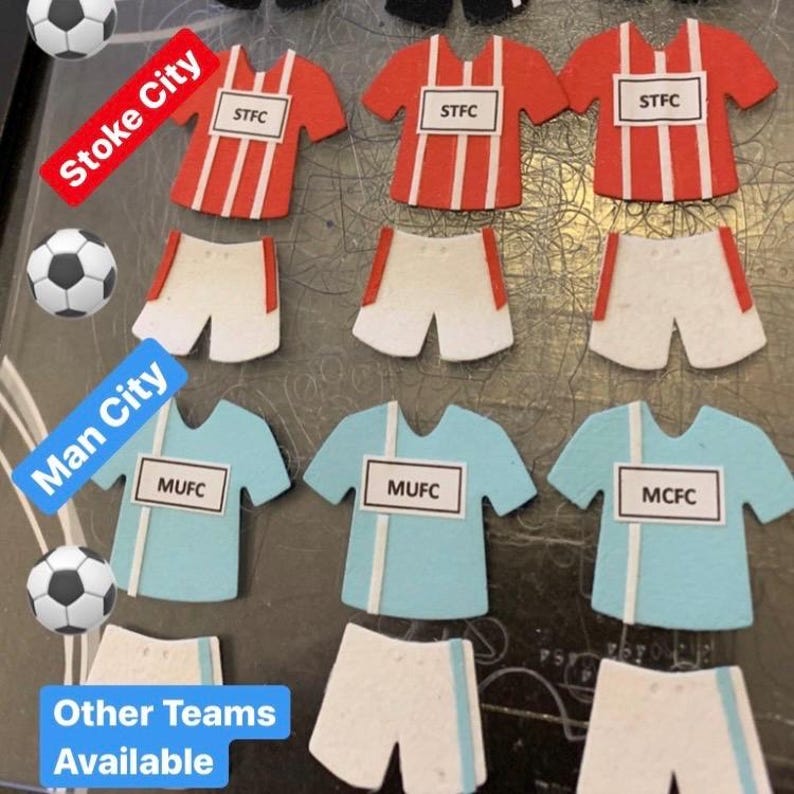 May include: A collection of felt football jerseys in various colors, including red, white, blue, and light blue. The jerseys have team names and logos, such as "Stoke City", "Man City", "STFC", "MUFC", and "MCFC".