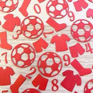 May include: Red paper cutouts of soccer balls, jerseys, shorts, socks, and numbers. The numbers include 0, 1, 2, 3, 4, 7, 8, and 9.