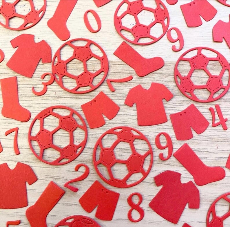 May include: Red paper cutouts of soccer balls, jerseys, shorts, socks, and numbers. The numbers include 0, 1, 2, 3, 4, 7, 8, and 9.