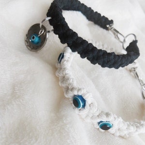 May include: Two braided cord bracelets with blue evil eye charms. One bracelet is black and the other is white.