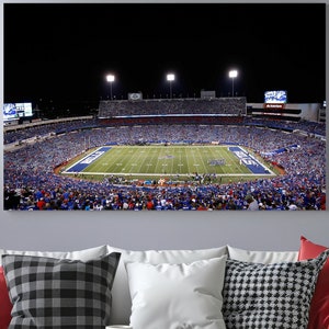 May include: A night time aerial view of a packed football stadium with a green field and a large scoreboard in the background.