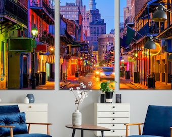 May include: A three-panel canvas print depicting a street scene in New Orleans at dusk. The street is lined with colorful buildings, and the streetlights cast a warm glow on the cobblestone street. The buildings are decorated with balconies and wrought iron railings. The print is a vibrant and colorful depiction of a classic New Orleans street scene.