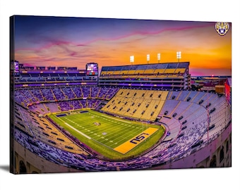 May include: An aerial view of a large football stadium with purple and yellow seats. The field is green with white lines and the word "LSU" is painted in the end zone. The sky is a vibrant orange and pink sunset.