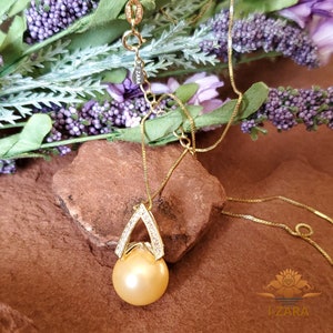 Puede incluir: Un collar de cadena de oro con un colgante que presenta una perla dorada grande rodeada por un marco de diamantes en forma de diamante de diamantes m&aacute;s peque&ntilde;os. El colgante cuelga de una delicada cadena de oro.