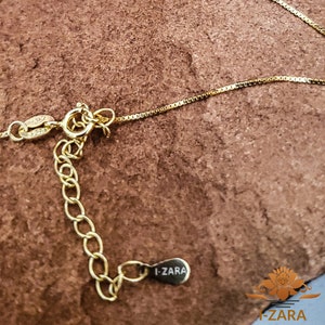 Puede incluir: Un collar de cadena de oro con un cierre de langosta y una cadena extensora. La cadena tiene un dise&ntilde;o de eslab&oacute;n de caja. El collar tiene una peque&ntilde;a etiqueta con el texto "I-ZARA" en ella.