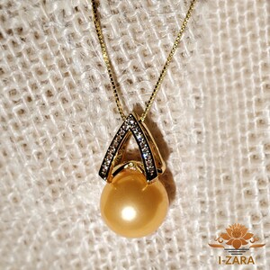 Puede incluir: Un collar de oro con un colgante que presenta una gran perla dorada y un marco de oro engastado con diamantes.