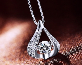 May include: A silver pendant necklace with a teardrop design. The pendant features a large, round, clear gemstone at the center, surrounded by smaller, sparkling stones. The necklace chain is also silver.