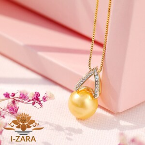 Puede incluir: Un collar de oro con un colgante de perla dorada y un peque&ntilde;o dije en forma de tri&aacute;ngulo engastado con piedras de circonita c&uacute;bica transparentes.