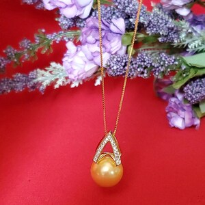Puede incluir: Un collar de cadena de oro con un colgante dorado que presenta una perla dorada grande, redonda. El colgante est&aacute; acentuado con peque&ntilde;os diamantes transparentes engastados en forma triangular.