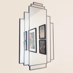 May include: A silver framed, rectangular mirror with a geometric design. The mirror is made up of multiple rectangular panels, each with a thin silver frame. The mirror is reflecting images of framed artwork.
