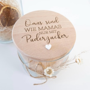 Könnte beinhalten: Ein Holz-Glas mit einem Deckel, auf dem "Omas sind wie Mamas nur mit Puderzucker" steht und ein kleines weißes Herz auf dem Deckel. Das Glas ist mit getrockneten Blumen gefüllt und mit einer Schnur gebunden.