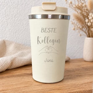 Könnte beinhalten: Ein cremefarbener Reisebecher mit passendem Deckel und silbernem Rand. Auf der Vorderseite befindet sich der Text "BESTE Kollegin" in einer Kombination aus Block- und Schreibschrift, eine Strichzeichnung von Händen in Herzform und der Name "Jana".