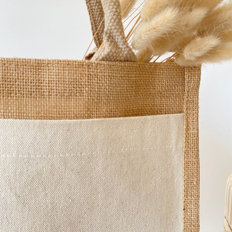 May include: A brown burlap tote bag with a white cotton bottom. The bag has a single handle and is made of natural materials.