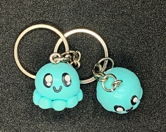 Könnte beinhalten: Zwei hellblaue Oktopus-Schlüsselanhänger mit lächelnden Gesichtern und schwarzen Augen. Die Oktopus-Schlüsselanhänger sind an silbernen Schlüsselringen befestigt.