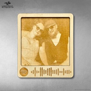 Könnte beinhalten: Eine Holzplakette mit einem lasergravierten Foto eines Paares, einem Spotify-Logo und einem Barcode. Das Foto zeigt einen Mann und eine Frau mit Sonnenbrillen. Die Plakette ist hellbraun.