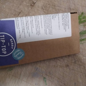 May include: A brown paper envelope with a blue and white label that says "Berry Tip-Top Farms". The envelope has a green leafy plant sticking out of the top.