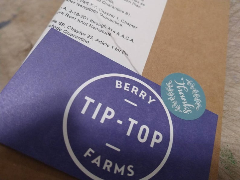 May include: A purple sticker with white text that reads "Berry Tip-Top Farms" in a circle. A teal sticker with white text that reads "Thanks" in a circle with a wreath design is on top of the purple sticker.